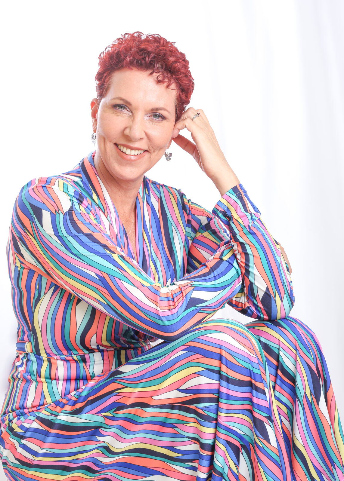Grace Walcott seated on a stool in a rainbow-striped outfit