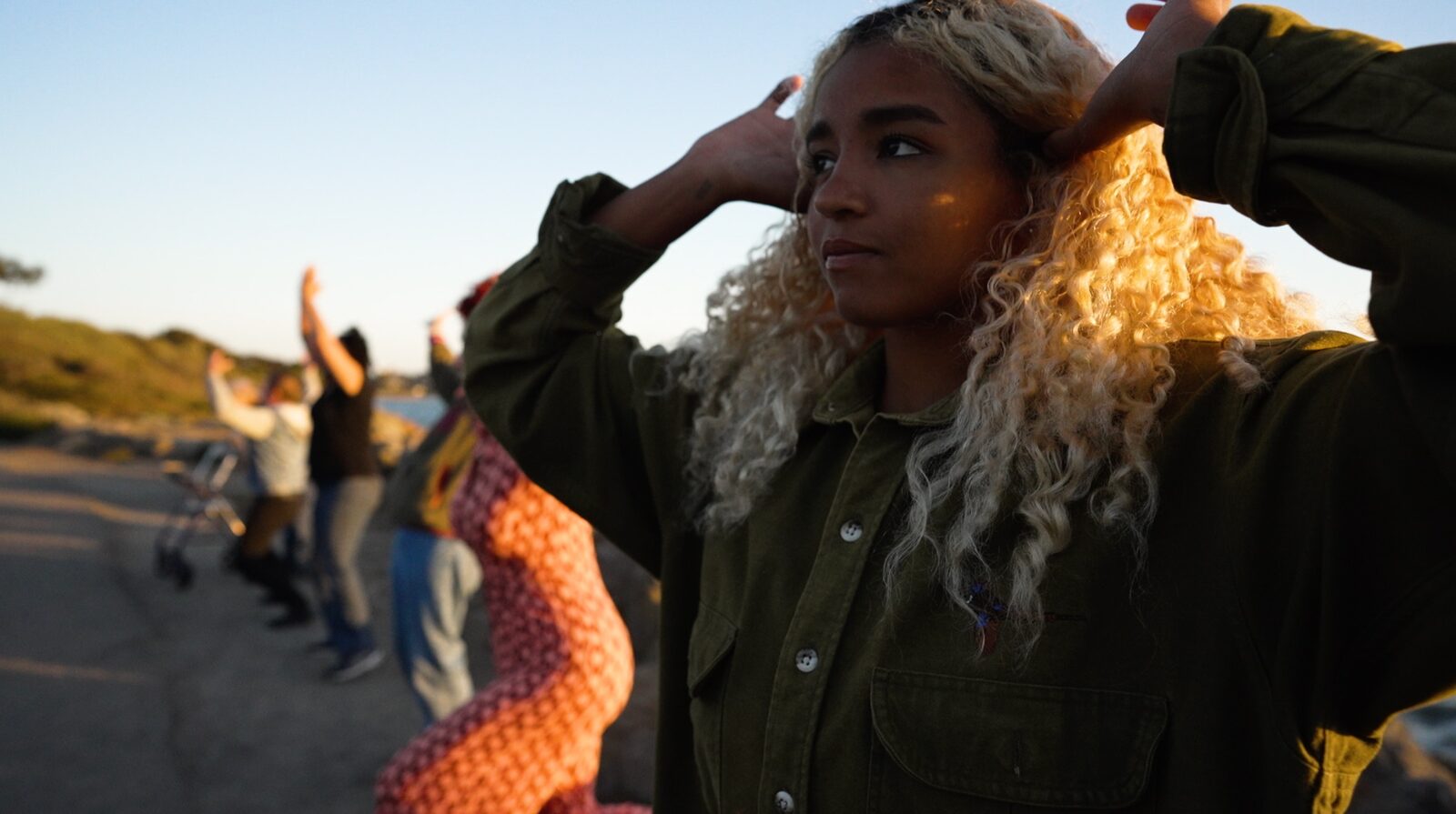 A participant outdoors at golden hour, hands lifted to their hair
