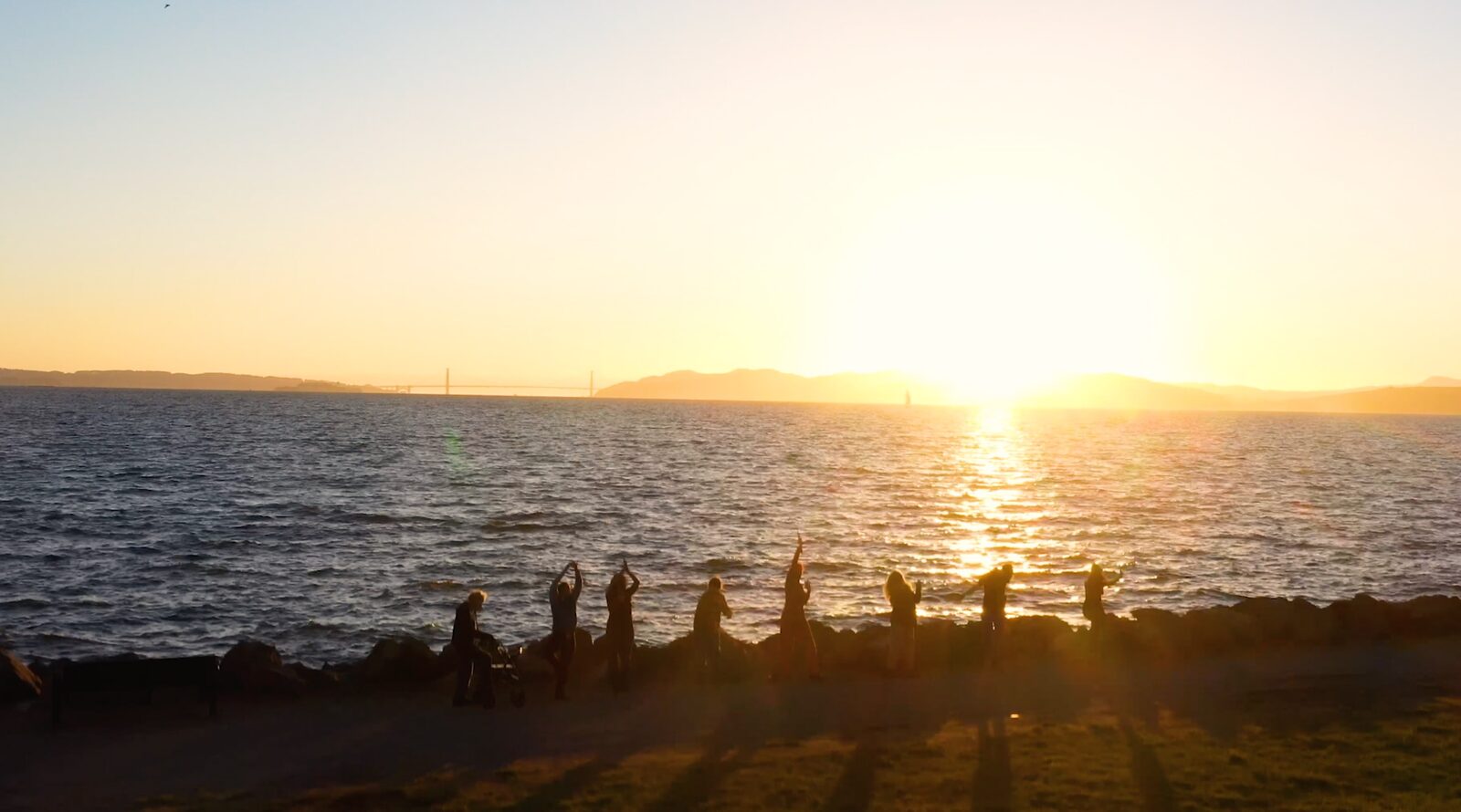 Participants silhouetted against the sunset over the bay